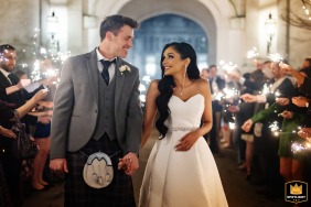 At Danesfield House, a wedding photographer captures a radiant exit. The image shows the bride and groom smiling as they exit, surrounded by guests holding sparklers.